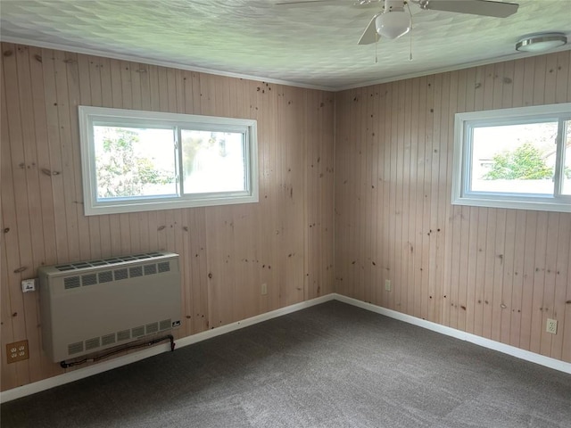 unfurnished room featuring ceiling fan, dark carpet, radiator heating unit, and wooden walls