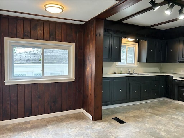 kitchen featuring beam ceiling, sink, and wooden walls