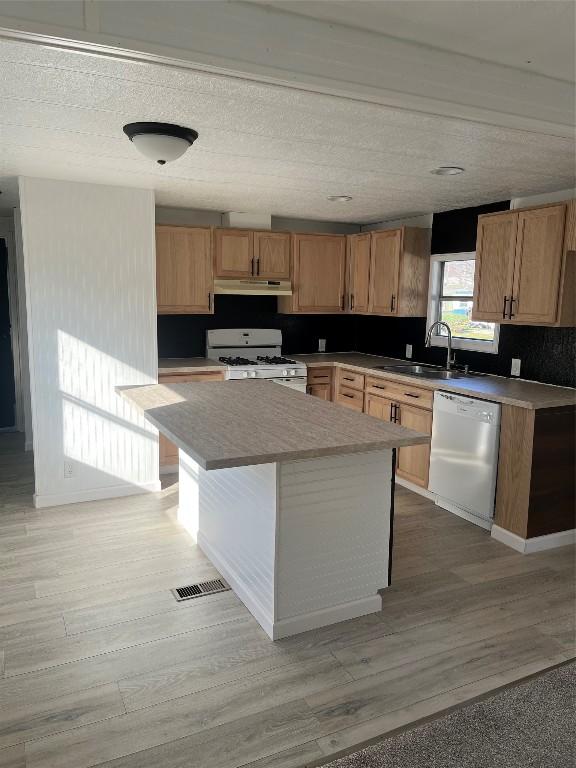 kitchen with sink, a kitchen island, white appliances, and hardwood / wood-style flooring