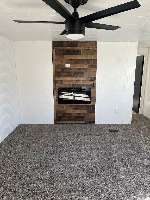 unfurnished living room with carpet, ceiling fan, and wooden walls