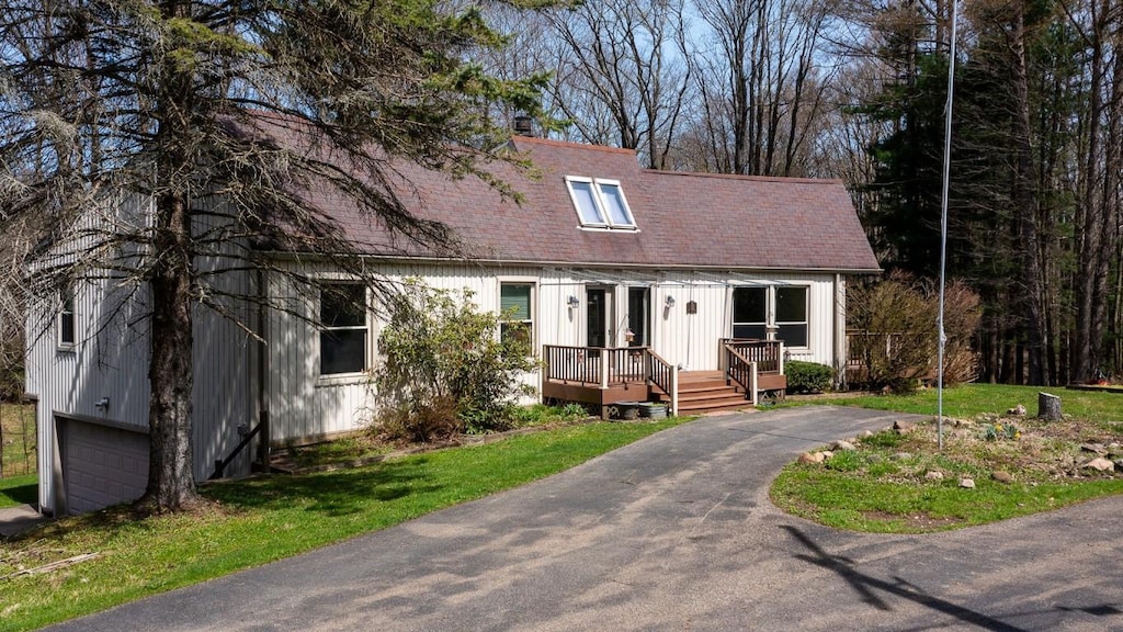 cape cod house with an attached garage, a shingled roof, and aphalt driveway