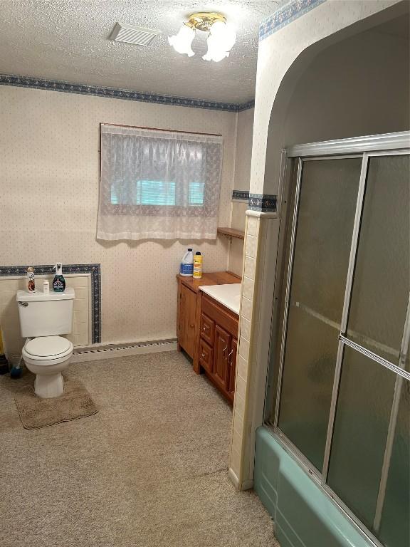 full bathroom featuring toilet, vanity, a textured ceiling, and combined bath / shower with glass door