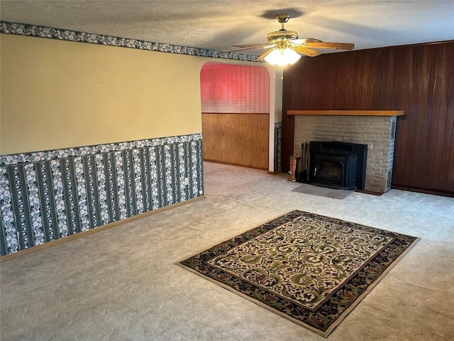 living room with ceiling fan, wood walls, light carpet, and a textured ceiling