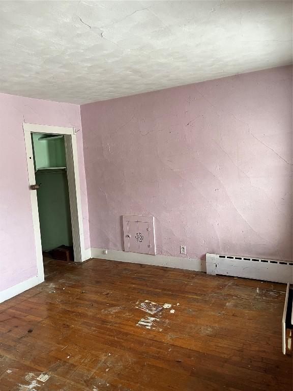 unfurnished room featuring dark hardwood / wood-style flooring and a baseboard heating unit