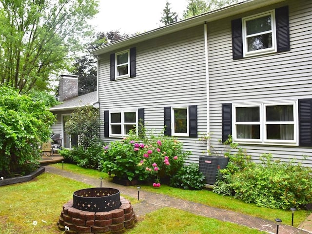 rear view of property featuring cooling unit, an outdoor fire pit, a yard, a chimney, and a deck