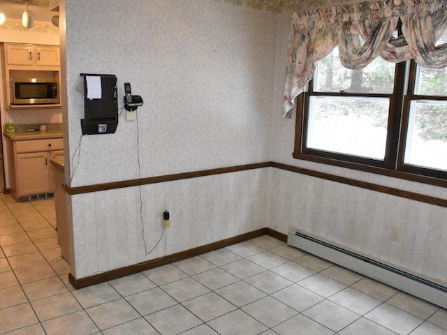 interior space with wallpapered walls, light tile patterned floors, baseboard heating, and wainscoting