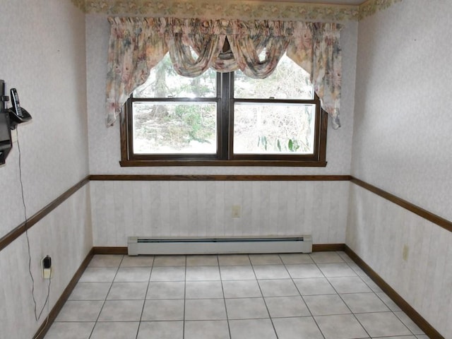 empty room featuring light tile patterned floors, baseboard heating, wainscoting, and wallpapered walls