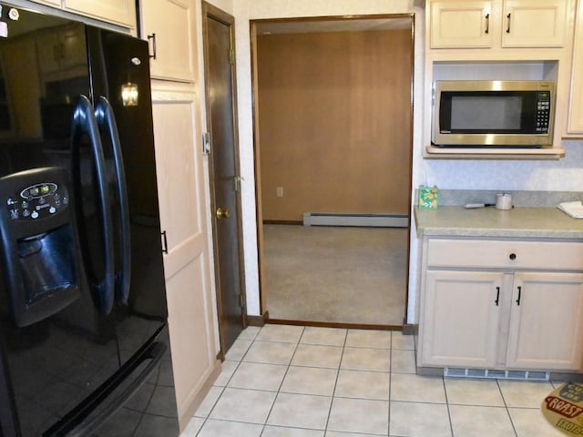 kitchen with stainless steel microwave, light countertops, light tile patterned floors, baseboard heating, and black refrigerator with ice dispenser