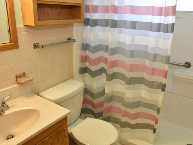 bathroom with tile walls, a shower with curtain, vanity, and toilet