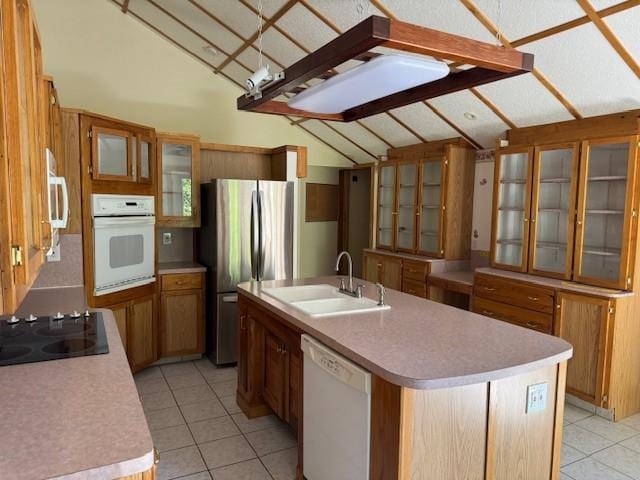 kitchen with white appliances, vaulted ceiling, a kitchen island with sink, sink, and light tile patterned flooring