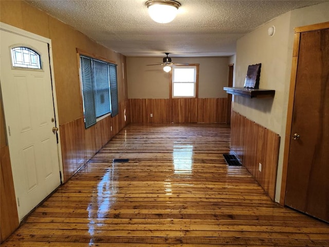 unfurnished living room with hardwood / wood-style flooring, ceiling fan, a textured ceiling, and wooden walls