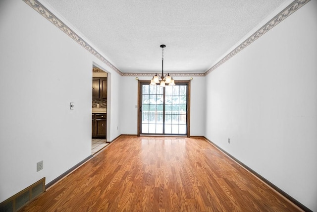 unfurnished dining area featuring a textured ceiling, light hardwood / wood-style flooring, ornamental molding, and an inviting chandelier