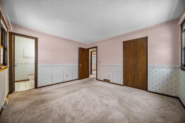 unfurnished bedroom featuring ensuite bathroom, a textured ceiling, and carpet floors