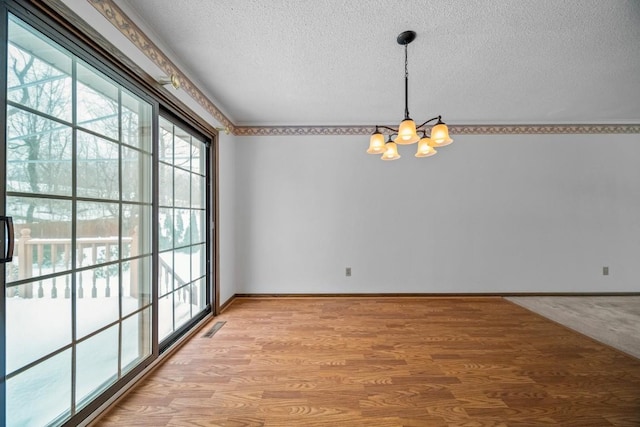 unfurnished dining area featuring a textured ceiling, light hardwood / wood-style flooring, and an inviting chandelier