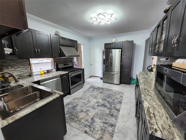 kitchen with appliances with stainless steel finishes, tasteful backsplash, wall chimney exhaust hood, light stone counters, and sink