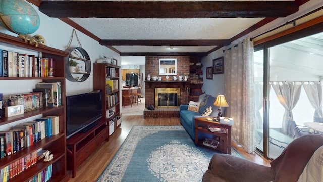 living room with beamed ceiling, wood-type flooring, a textured ceiling, and a brick fireplace