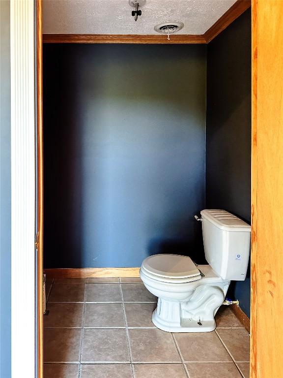 bathroom with tile patterned floors, toilet, a textured ceiling, and ornamental molding