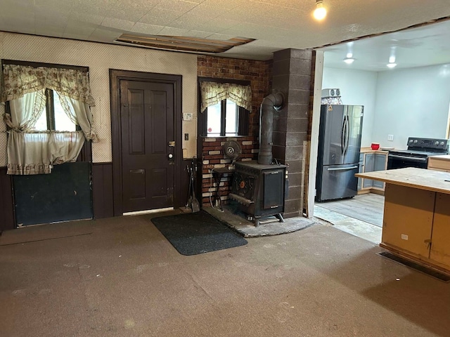 interior space with light colored carpet, a wood stove, stainless steel refrigerator, and black / electric stove