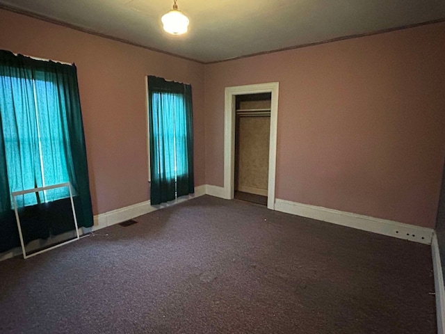 unfurnished bedroom featuring dark carpet, multiple windows, and a closet