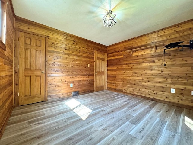 unfurnished room featuring visible vents, wooden walls, and light wood finished floors