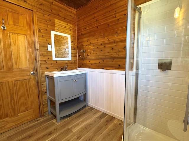 full bathroom featuring wood finished floors, wainscoting, wood walls, vanity, and a stall shower