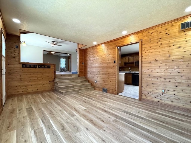 unfurnished living room with a textured ceiling, visible vents, wood walls, and light wood-type flooring