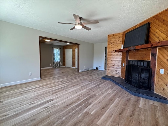 unfurnished living room featuring baseboards, visible vents, ceiling fan, and wood walls