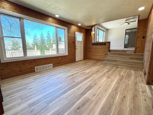 unfurnished living room featuring light wood-style floors, visible vents, a textured ceiling, and wood walls