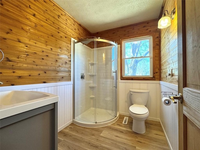 full bathroom with toilet, a textured ceiling, a shower stall, and wood walls