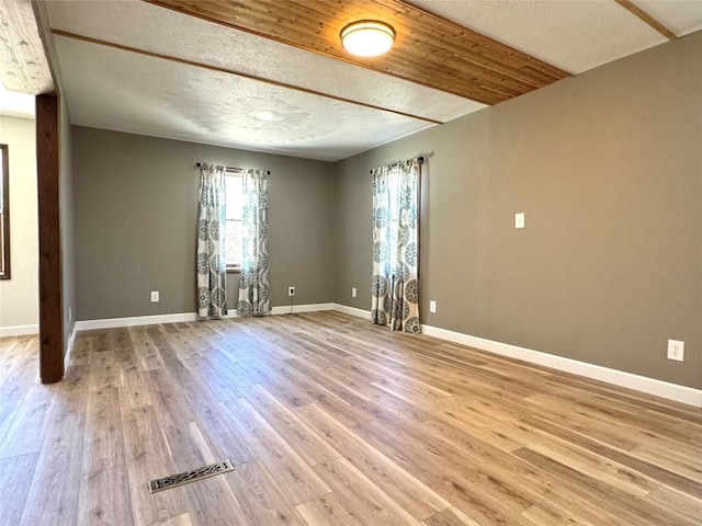 spare room with a textured ceiling, visible vents, light wood finished floors, and baseboards