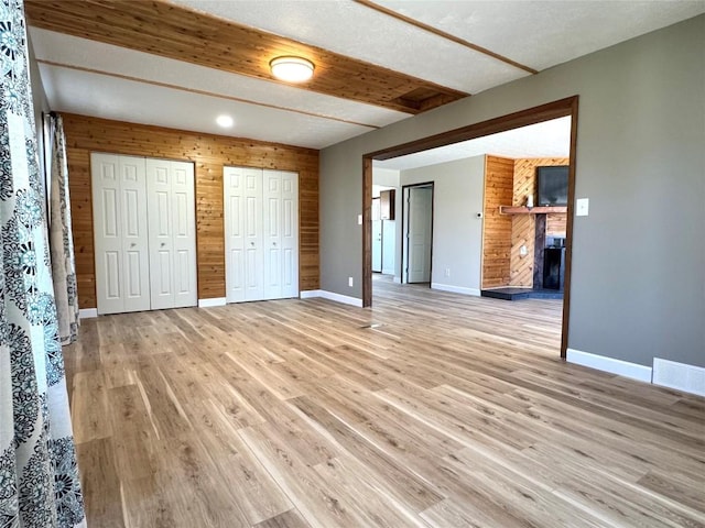 unfurnished bedroom with a large fireplace, light wood-style floors, multiple closets, baseboards, and visible vents