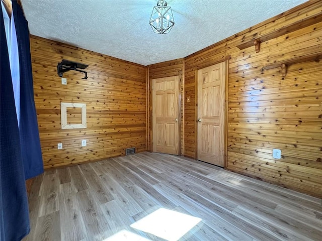unfurnished room with visible vents, wood finished floors, a textured ceiling, and wood walls