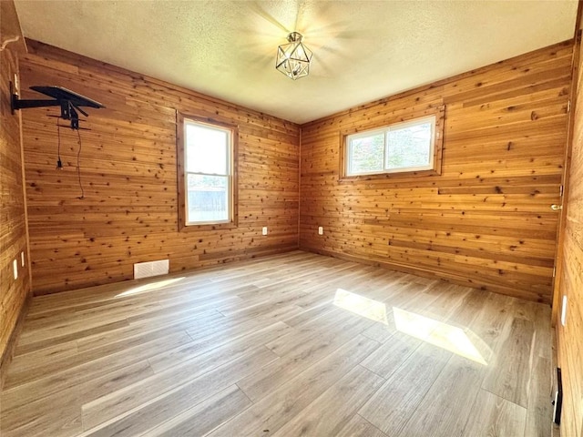 empty room with wooden walls, a textured ceiling, and light wood finished floors