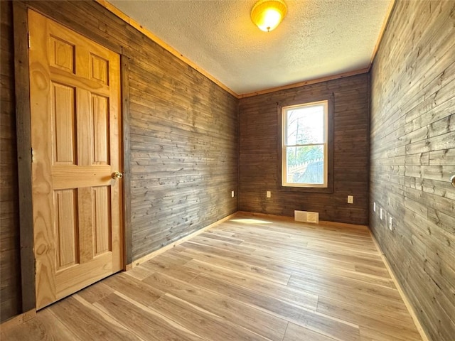 empty room featuring light wood-style floors, visible vents, wooden walls, and a textured ceiling