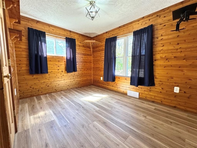unfurnished room featuring wooden walls, wood finished floors, visible vents, and a textured ceiling