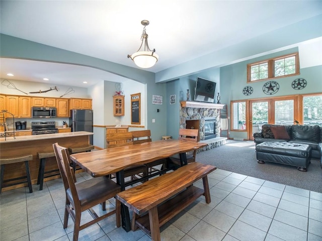 dining room featuring recessed lighting, a stone fireplace, light carpet, light tile patterned floors, and arched walkways