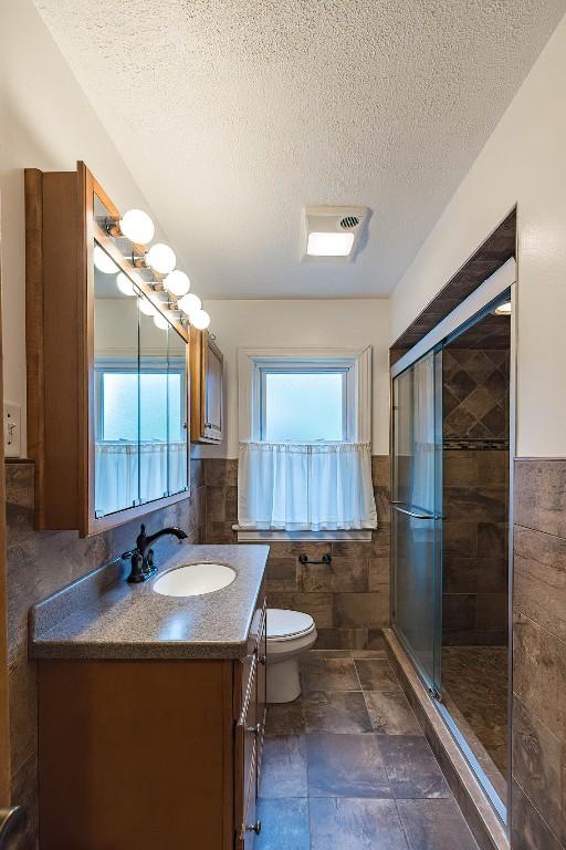 bathroom featuring a textured ceiling, vanity, tile walls, and a shower with shower door