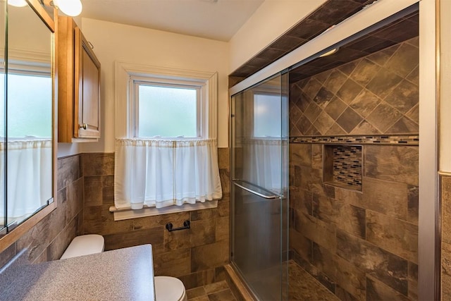 bathroom with vanity, a shower with shower door, tile walls, and toilet