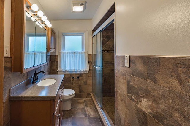 bathroom with a shower with door, vanity, tile walls, and toilet