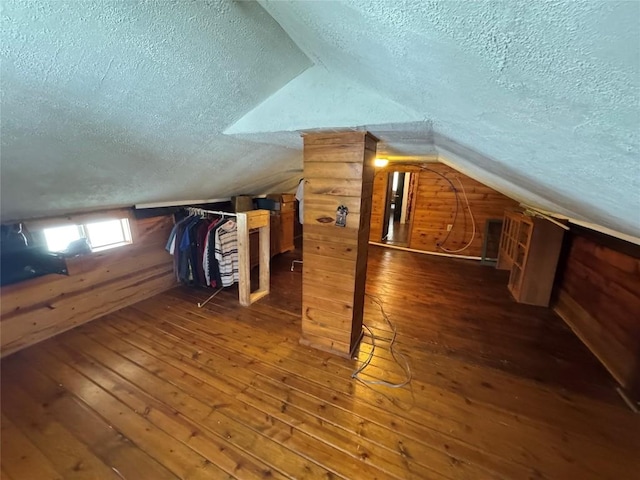 additional living space with a textured ceiling, dark hardwood / wood-style flooring, lofted ceiling, and wooden walls