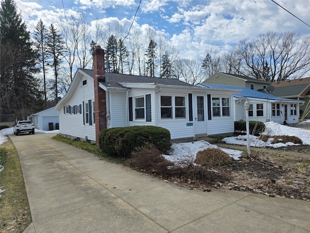 view of front of home featuring a shingled roof, an outbuilding, a detached garage, and a chimney