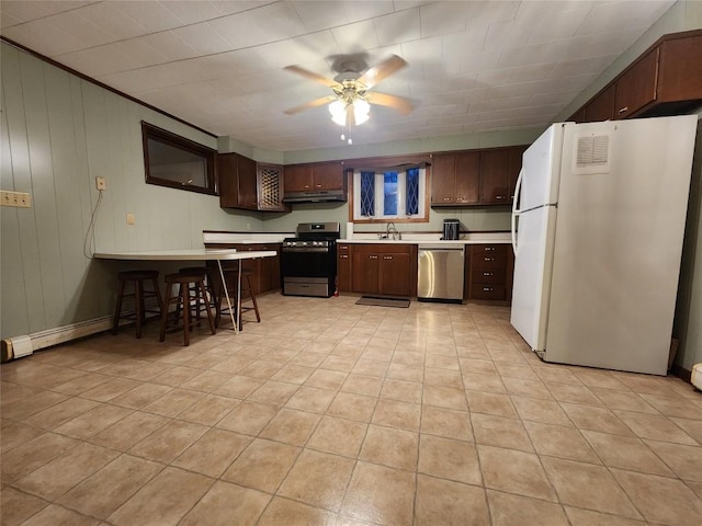 kitchen with ceiling fan, sink, stainless steel appliances, wooden walls, and dark brown cabinets