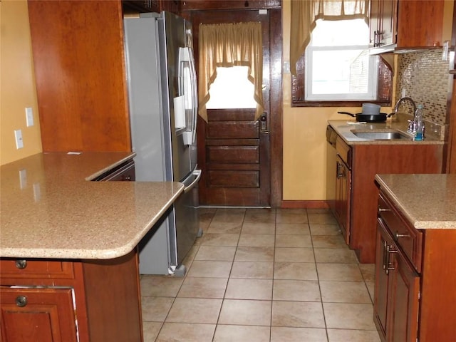 kitchen with light tile patterned flooring, sink, stainless steel fridge, kitchen peninsula, and decorative backsplash