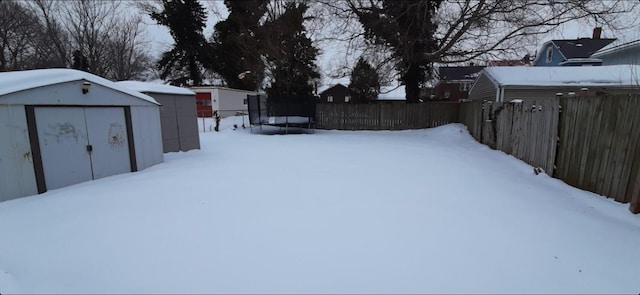 yard covered in snow featuring a trampoline and a storage shed