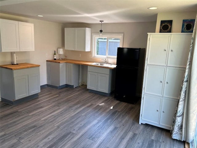 kitchen featuring wood counters, black fridge, dark wood-type flooring, sink, and white cabinets