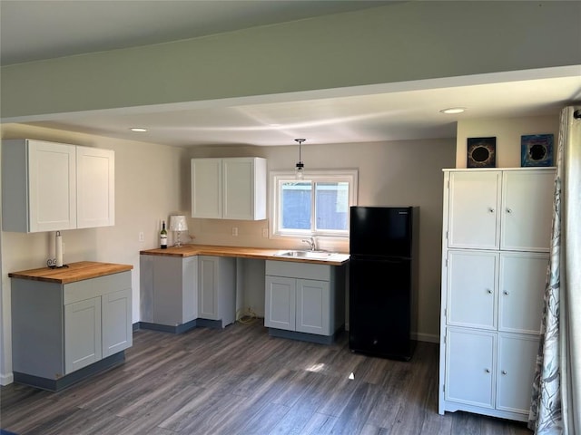 kitchen featuring dark wood-type flooring, white cabinets, black fridge, sink, and butcher block counters