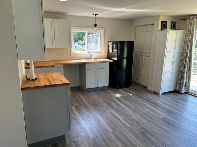 kitchen featuring wood counters, black fridge, sink, pendant lighting, and dark hardwood / wood-style floors