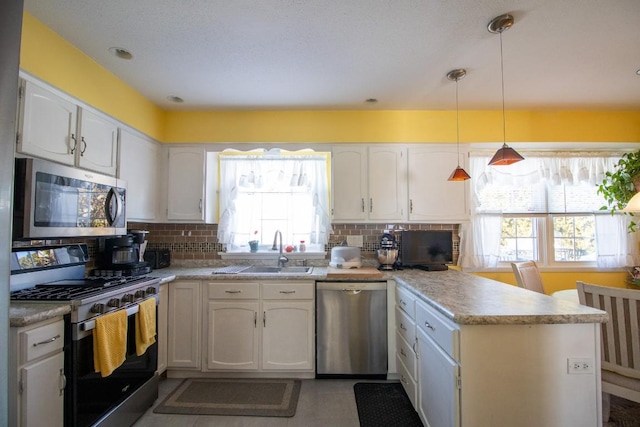 kitchen with appliances with stainless steel finishes, kitchen peninsula, white cabinets, and decorative light fixtures