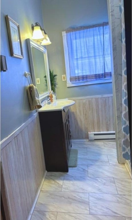 full bath with wood walls, a baseboard radiator, vanity, and wainscoting