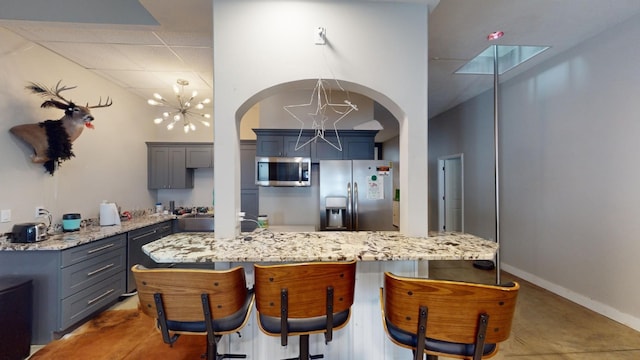 kitchen with stainless steel appliances, light stone countertops, a towering ceiling, and a notable chandelier